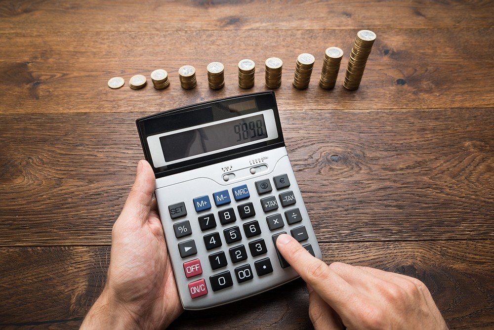 Калькулятор в руках и стопки монет на столе